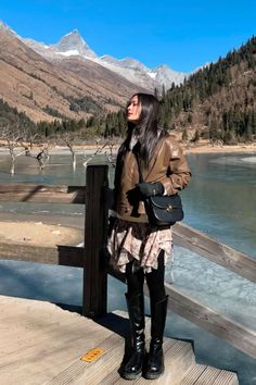 a woman is standing on a dock by the water with mountains in the back ground