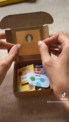 two hands holding an open cardboard box with stickers and magnets on the inside