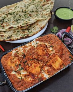 some food is sitting on a table next to other foods and condiments, including naan bread