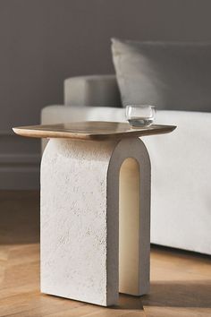 a white table with a glass on it in front of a couch and coffee table