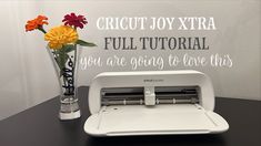 a white cricut joy xtra machine sitting on top of a table next to a vase with flowers