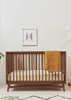 a baby crib in a white room with a yellow blanket on it's bed