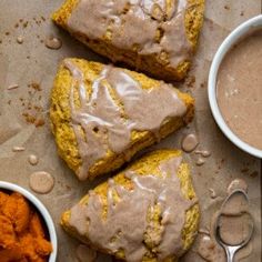 three pieces of bread with frosting on them next to bowls of carrots and dipping sauce