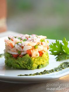 a white plate topped with guacamole covered in shrimp and cilantro