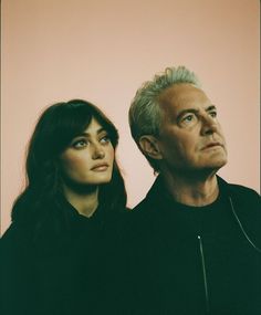 two people standing next to each other in front of a pink wall with one person looking up