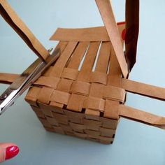 a person cutting paper with scissors on top of a wooden basket that is made out of cardboard