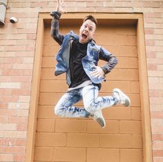 a man jumping up into the air with his arms wide open in front of a brick wall