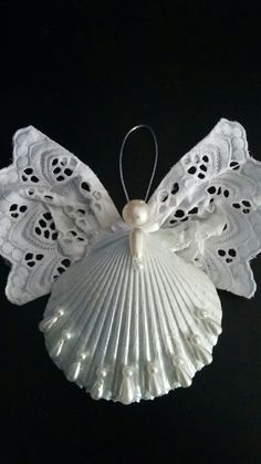 a white angel ornament hanging from a black background with lace and pearls on the wings