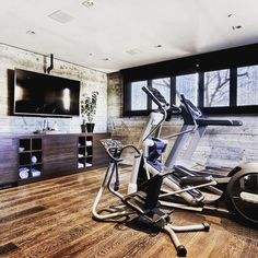 an exercise room with treadmills, television and large windows in the back wall