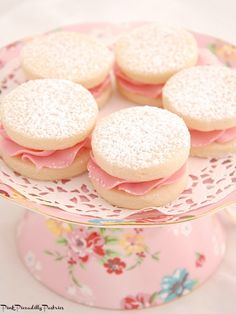 small cookies with pink frosting on top of a flowered cake plate and cupcakes in the background