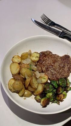 a white plate topped with meat and vegetables next to a fork on a table top