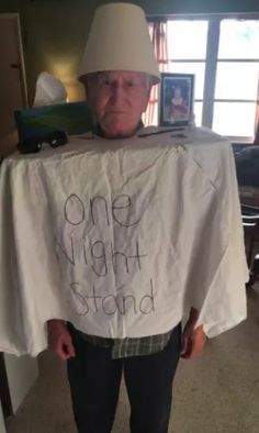 an older man wearing a white hat and holding up a t - shirt that says one night stand