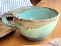 a green cup sitting on top of a wooden table next to a plate and bowl