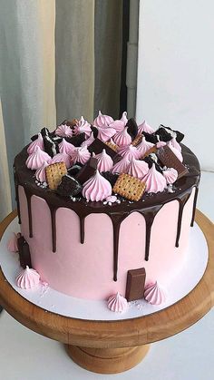 a chocolate and pink cake with cookies on top is sitting on a wooden platter