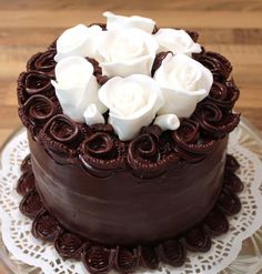 there is a chocolate cake with white roses on the top and bottom, sitting on a lace doily