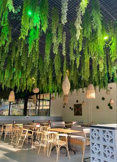 an indoor restaurant with tables and chairs covered in green plants hanging from the ceiling above