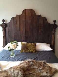 a bed with a wooden headboard and pillows on top of it, next to a vase filled with flowers