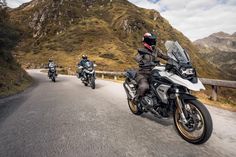 three people riding motorcycles down a mountain road