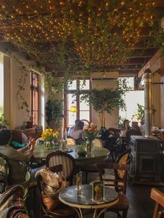 people sitting at tables in a restaurant with plants hanging from the ceiling