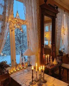 a dining room table with candles lit in front of a large window overlooking the snow covered trees