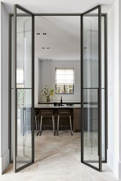 an open glass door leading to a kitchen and dining room with two chairs in it