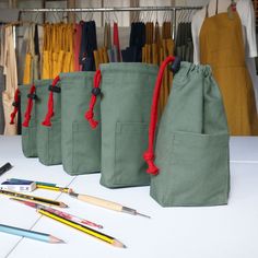 several pencils and markers are lined up in front of three green bags with red handles