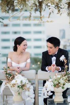 a man and woman sitting next to each other at a table with flowers in vases