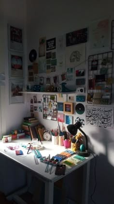 a white desk topped with lots of clutter and art supplies next to a wall covered in pictures