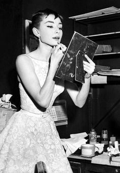 a black and white photo of a woman in a dress holding an open book while looking at it