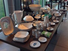 a long table with plates and cups on it in front of a large glass window