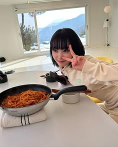 a woman making the peace sign with her hand while holding a frying pan full of spaghetti