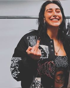 a woman with black hair and piercings holding up two fingers