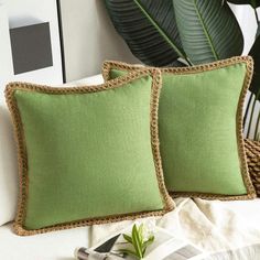 two green pillows sitting next to each other on a bed with plants in the background