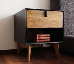 a wooden cabinet with two red books on it next to a gray chair and white wall