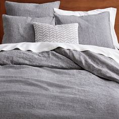 an unmade bed with grey linens and white pillows