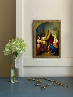 a painting on the wall next to a vase with flowers in it and a rosary