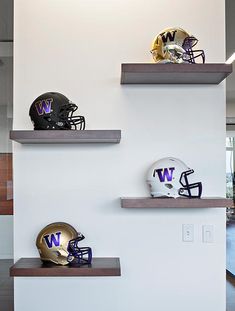 three football helmets are sitting on shelves in a room with white walls and wood flooring