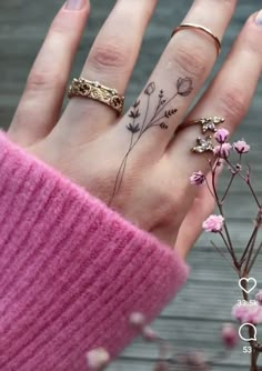 a woman's hand with tattoos on her fingers and flowers in the middle of it