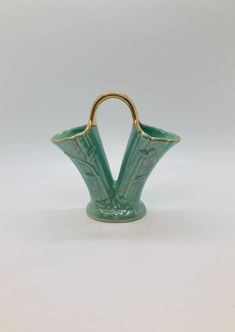 a green vase sitting on top of a white table next to a wooden handle with two handles