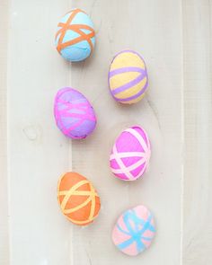 four decorated easter eggs sitting on top of a white table next to an orange, pink and blue striped egg