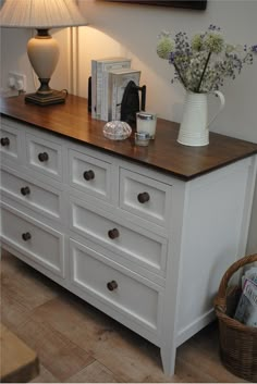 a white vase with flowers on top of a dresser