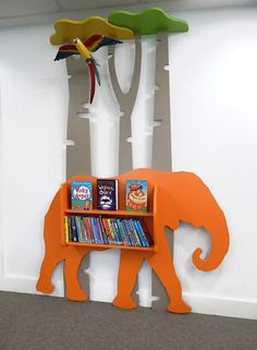 an orange book shelf with books on it in front of a wall mounted elephant and trees