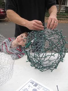 a man is working on a wire ball with a young boy sitting next to it