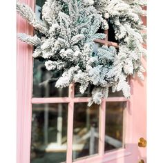 a wreath hanging on the side of a pink door with frosted pine branches in it