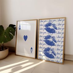 two framed pictures with blue ink on them next to a potted plant and window