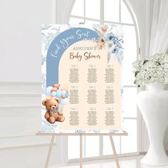 a baby shower sign with a teddy bear on it next to a vase and flowers