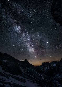 the night sky is filled with stars above mountains and snow covered ground, as well as some rocks