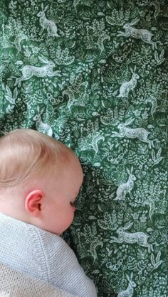 a baby laying on top of a bed next to a green and white wallpaper