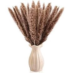 a white vase filled with dried grass on top of a table