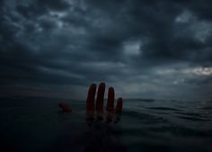 two fingers sticking out of the water under a dark sky with clouds in the background